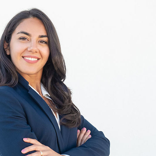 Smiling confident businesswoman posing with arms folded. Happy beautiful black haired young Latin woman in formal suit standing for camera over white studio background. Corporate portrait concept